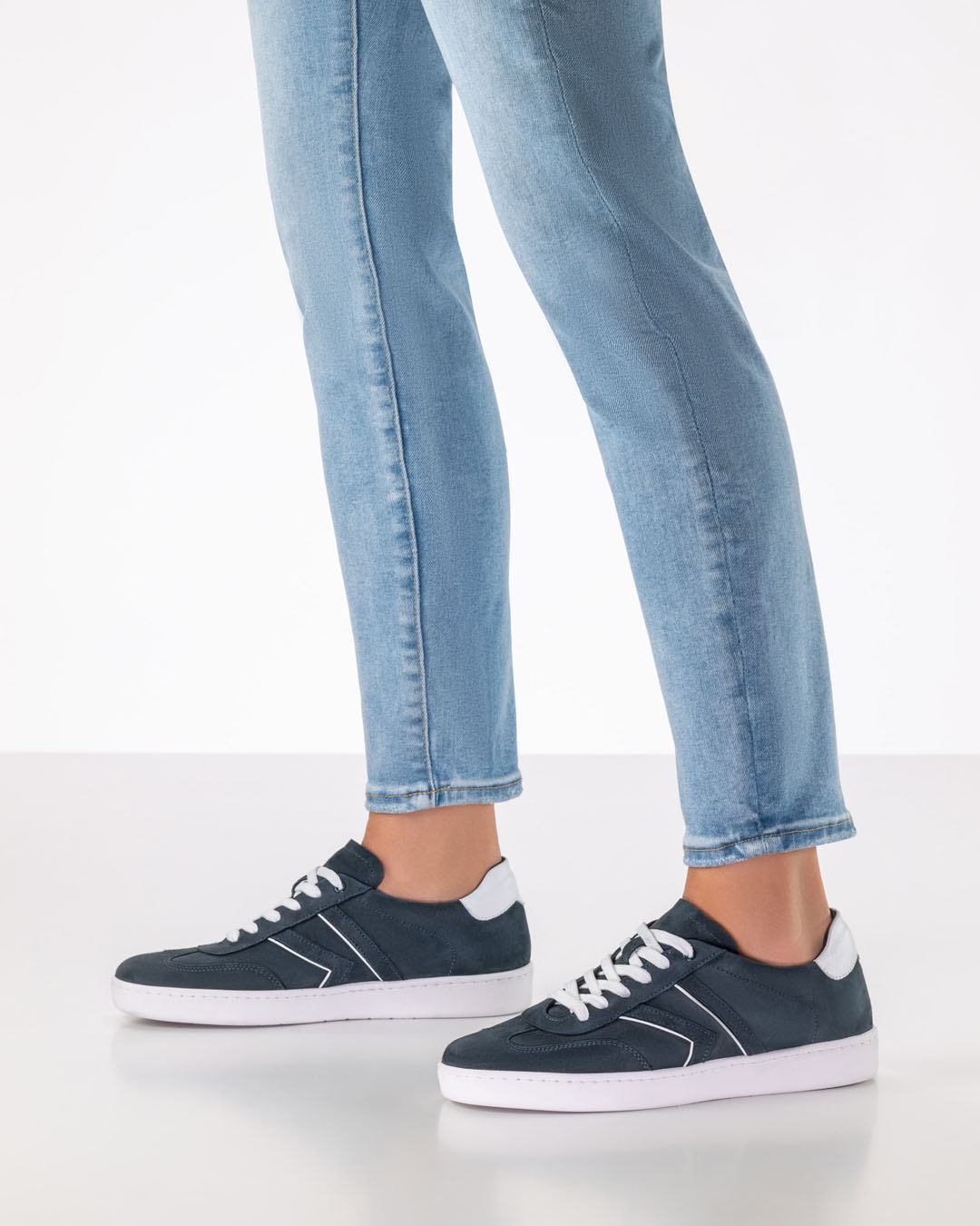 Modell steht seitlich und trägt eine helle, schmale Jeans und dunkelblaue Velourledersneaker mit weißer Sohle