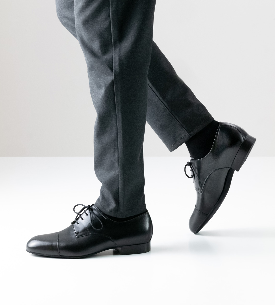 Herrentanzschuh in schwarzem Leder mit 2 cm hohem Absatz in Kombination mit grauer Hose