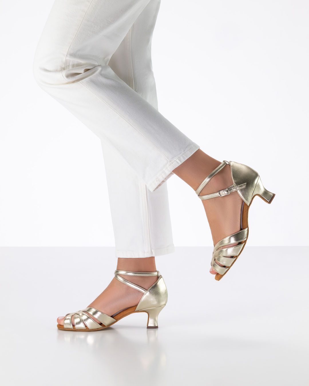 Modell steht seitlich und hebt einen Fuß nach hinten hoch mit goldenen Tanzsandalen von Anna Kern.