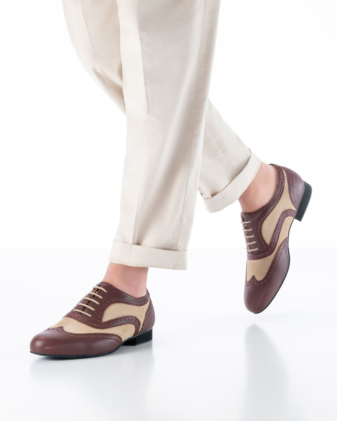 Herrenmodel in cremfarbener Hose läuft zur Kamera mit Tanzschuhen in caramel und bordeaux mit Brogue Lochmuster