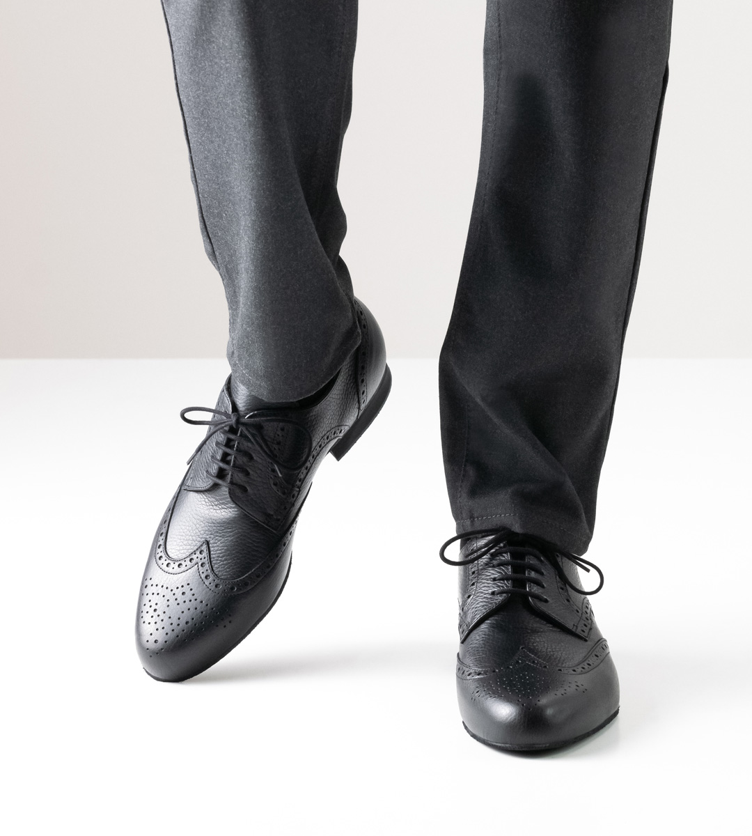 Herrentanzschuh in schwarzem Leder mit 2 cm hohem Absatz in Kombination mit grauer Hose